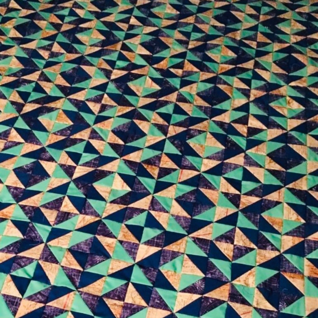 Quilt with intricate pattern of right triangles with tan, mint green, and navy