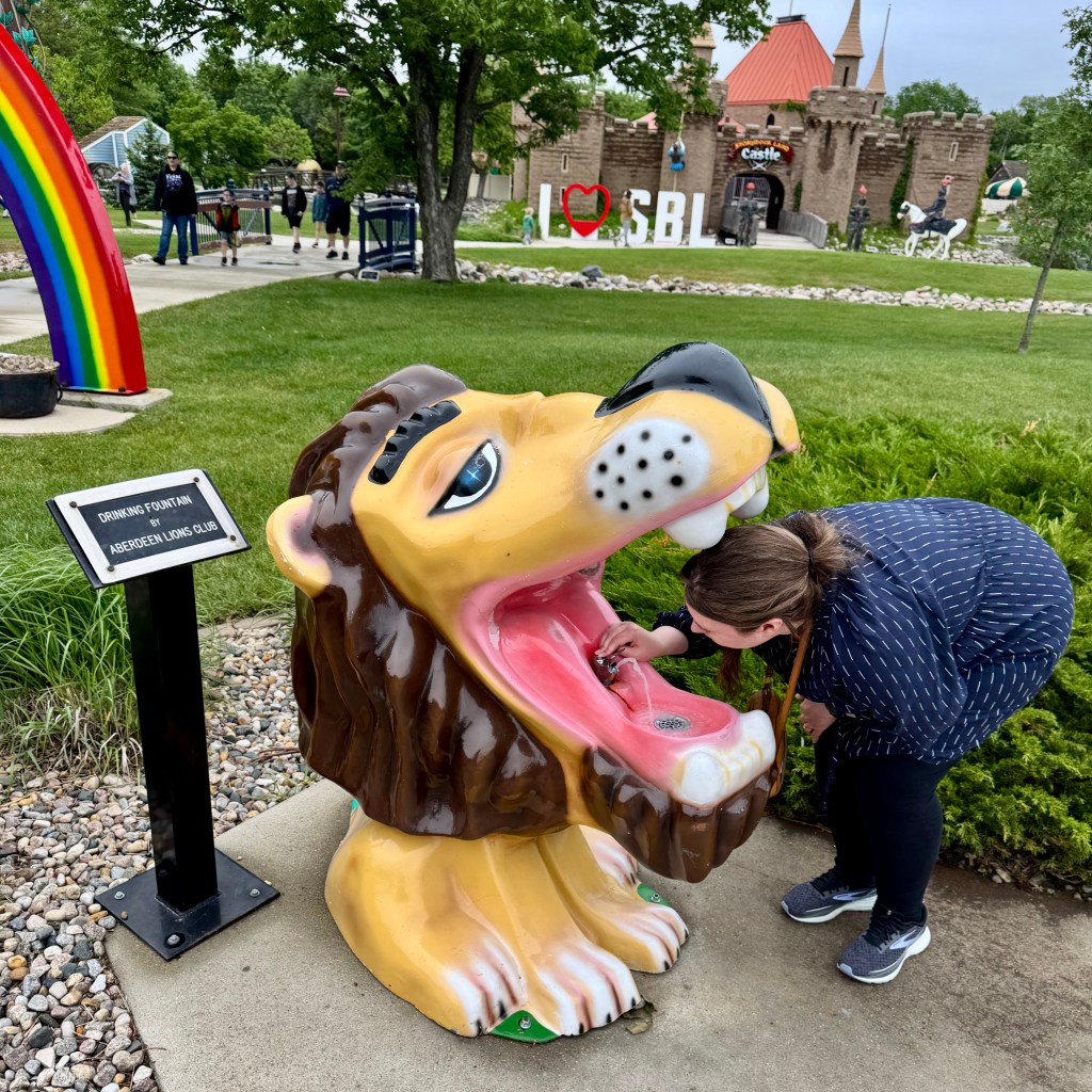 Alexandra leaning with her head inside a large lion's mouth that is actually a water fountain.
