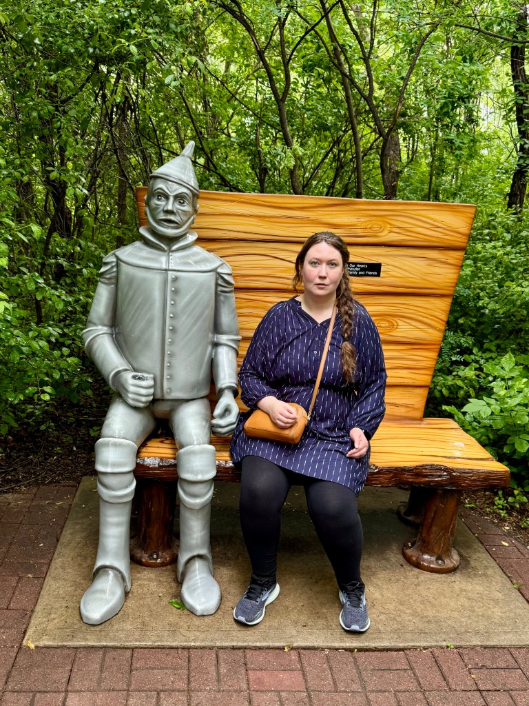 Alexandra sitting on a bench next to a statue of the Tin Man.